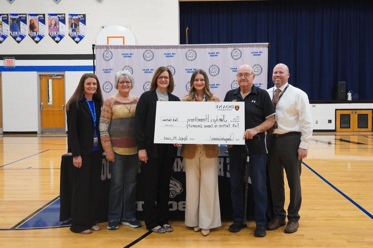 Jaelyn Himmelberg holds up a giant check to celebrate receiving Doane's Academic Excellence scholarship. With her are her family and Blue Hill High School administrators, including four-time Doane grad, Principal Patrick Moore '03, '07E, '11E, '18E (far left).